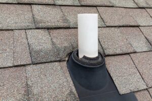 A close-up of a roofing contractor examining shingles on a sloped roof with tools and safety harness.
