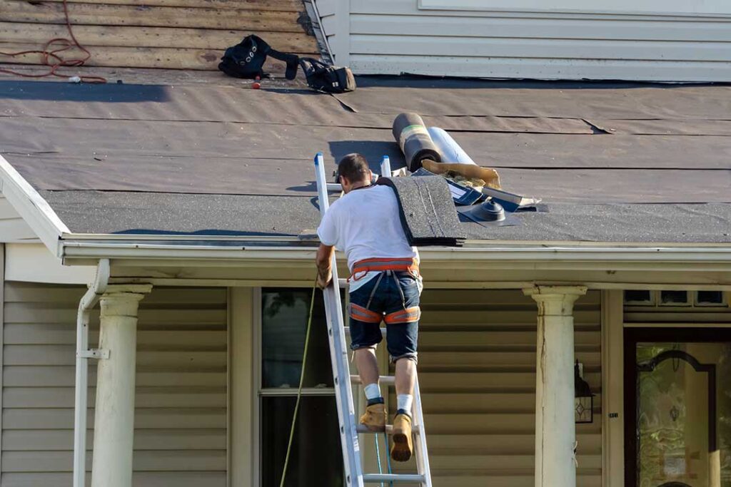 A roofer fitting metal flashing around a vent pipe on a shingled residential roof.